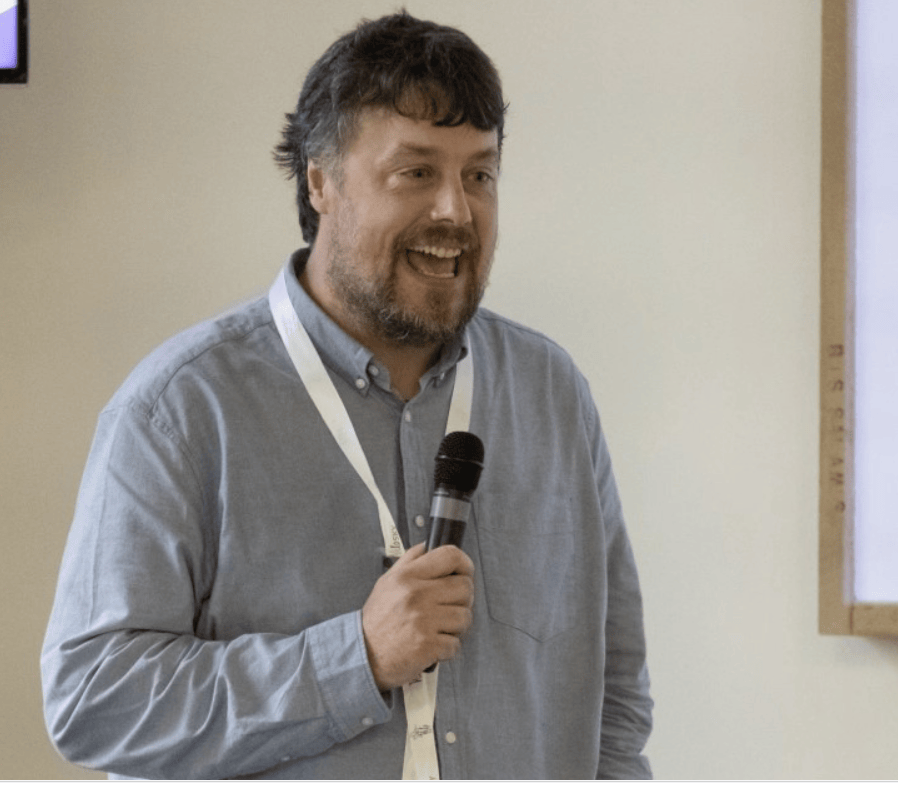 Chris McGuire speaking at an author event, holding a microphone.